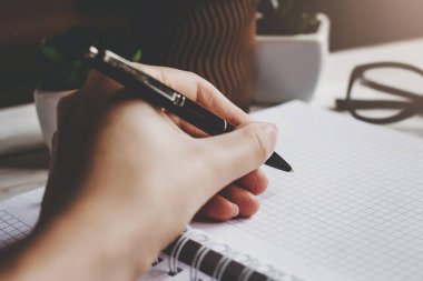 Kadın bir kalem tutuyor ve bir deftere yazıyor, koyu arkaplan. Solak kız not defterine notlar alır, koyu tonlu fotoğraf.