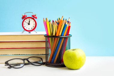 Okul konseptine geri dönelim. Kırmızı alarm, elma, renkli kalemler, mavi arka planda kitaplar. 1 Eylül konsepti.