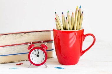 1 Eylül konsepti. Kırmızı alarmlı saat, bardak, renkli kalemler, beyaz ahşap arka planda kitaplar. Okul konseptine dönelim.