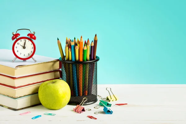 Back to school concept. Red alarm clock, apple, color pencils, books on a blue background. September 1st concept.