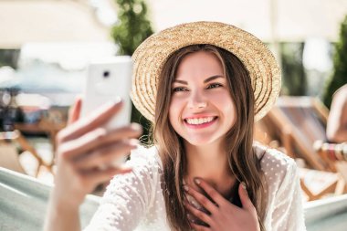 Yazın plajda hasır şapkayla oturan kız çok utanmış ve gülümsüyor.