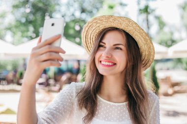 Yaz kıyafetleri içinde genç bir kadının portresi, özçekim yapan hasır şapka, video konferans, internet üzerinden telefon görüşmeleri ve koronavirüs karantinası sırasında video görüşmeleri.