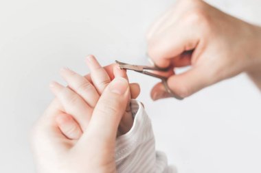 Bebek manikürü. Anne, bebeğin tırnaklarını özel bir çocuk makasıyla kesiyor. Kapat. Yeni doğanlar için manikür. beyaz arkaplan