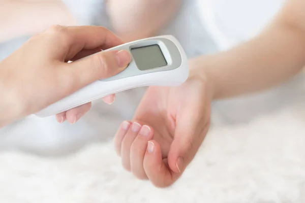A woman\'s hand applies an infrared thermometer to measure body temperature. High fever with flu and colds. Coronavirus prevention. Body temperature measurement at home. Health care. Viral infection