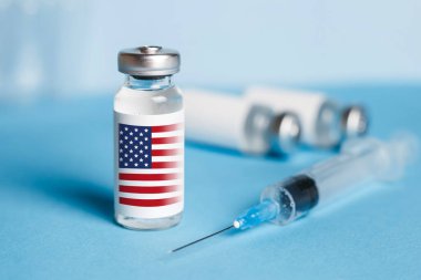 Amerikan aşısı konsepti. Mavi arka plan ve şırınga üzerinde covid-19 'dan enjekte edilmiş ampul.