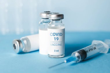 Coronavirus aşısı. Koronavirüs aşısıyla ampuller ve mavi arka planda bir şırınga. Covid-19 tedavisi