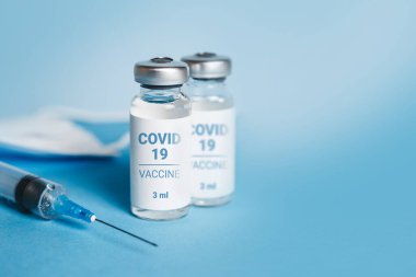 Coronavirus aşısı. Koronavirüs aşısıyla ampuller ve mavi arka planda bir şırınga. Covid-19 tedavisi. Boşluğu kopyala