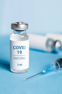 Coronavirus aşısı. Koronavirüs aşısıyla ampuller ve mavi arka planda bir şırınga. Covid-19 tedavisi. Dikey biçim