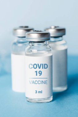 Coronavirus aşısı. Koronavirüs aşısıyla ampuller ve mavi arka planda bir şırınga. Covid-19 tedavisi. Dikey biçim