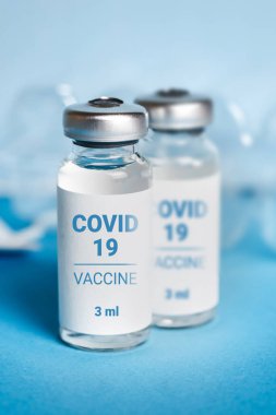 Coronavirus aşısı. Koronavirüs aşısıyla ampuller ve mavi arka planda bir şırınga. Covid-19 tedavisi