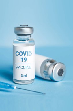 Coronavirus aşısı. Koronavirüs aşısıyla ampuller ve mavi arka planda bir şırınga. Covid-19 tedavisi