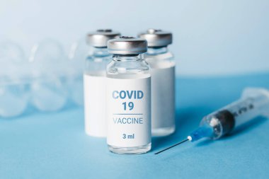 Coronavirus aşısı. Üç ampul koronavirüs aşısı ve mavi arka planda bir şırınga. Covid-19 tedavisi