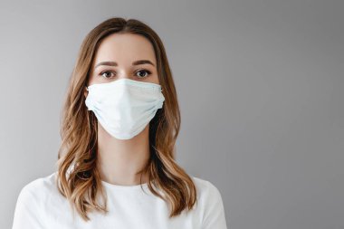 Beyaz arka planda izole edilmiş tıbbi maskeli genç bir kızın portresi. Genç kadın hasta gri arka planda duruyor, kopyalama alanı