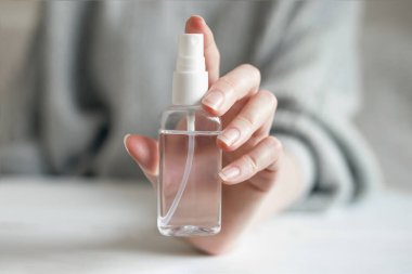 Kadın elinde bir şişe dezenfektan jeli, koronavirüs bakterisinden alınan antibakteriyel alkol spreyi mavi arka planda izole edilmiş, covid 19, el hijyeni.