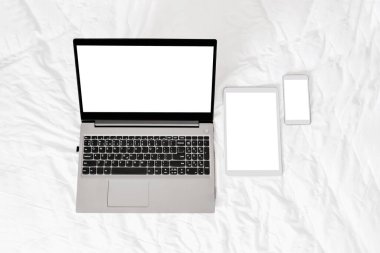 Beyaz arka planda beyaz dijital tabletli ve akıllı telefonlu gri dizüstü bilgisayarı aç. Tablet ve telefon beyaz ekranlı. Model modeli. Tasarım için kopyalama alanı. en üstteki görünüm