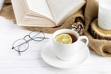 Çay, kitap, bardak, mum beyaz ahşap bir masada.