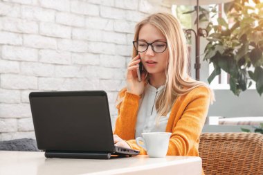 Dizüstü bilgisayarda çalışan genç bir kız. Kafede dizüstü bilgisayarı ve kahvesi olan sarışın bir kız.