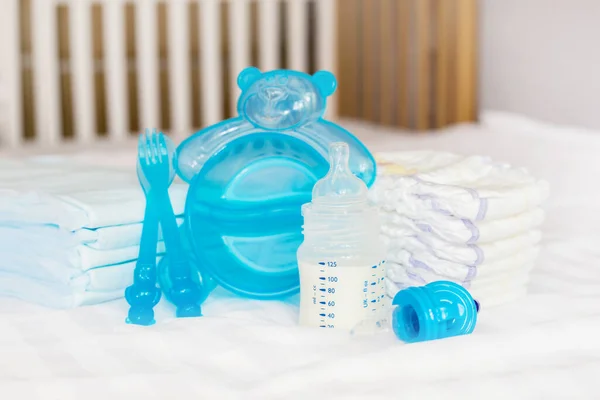 赤ちゃんの透明なプラスチック料理のセット ミルクボトル ニンブラー ブルーカトラリー スプーン フォーク オムツ おもちゃ 使い捨ておむつを白いベッドの背景に供給しています 健康的な栄養 — ストック写真