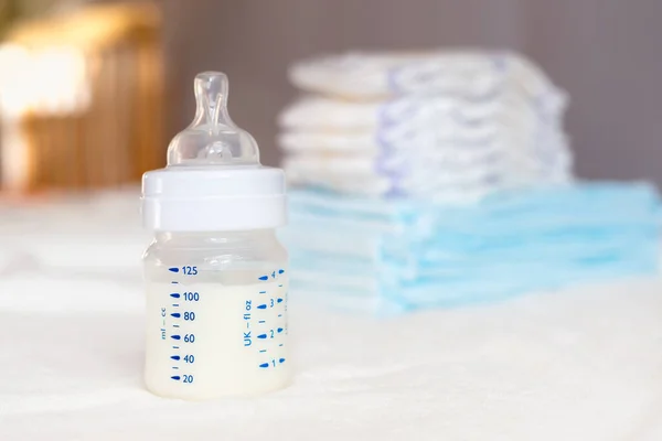 白い生地の背景にミルクとおむつ付きのベビーボトル 赤ん坊の世話だ 人生の最初の日 養育と母親 使い捨て吸湿式衛生用紙 — ストック写真
