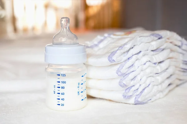 白い生地の背景にミルクとおむつ付きのベビーボトル 赤ん坊の世話だ 人生の最初の日 食生活と母性 — ストック写真