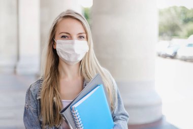 Kafkas öğrenci portresi, tıbbi maske takan ve eski bir üniversite binasının arka planına karşı not defterleri tutan, Coronavirus 'tan sonra yeni sosyal kurallar konan,