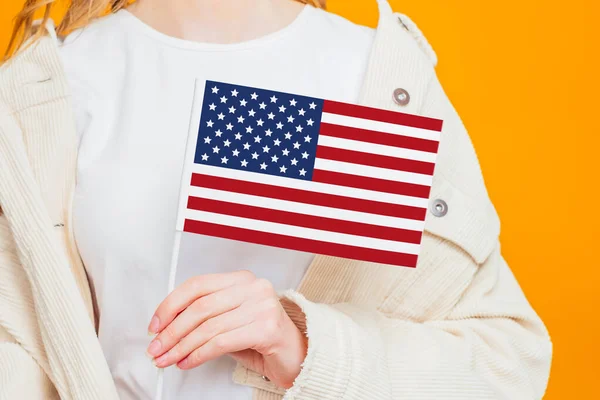 Female hand holds America flag isolated over orange background, holding USA flag, 4th of july independence day