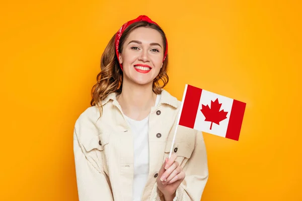 年轻的女学生笑着举着小加拿大国旗 在橙色的背景下把目光投向远方 加拿大日 邦联周年纪念日 复制空间 — 图库照片