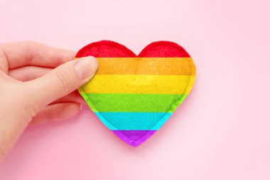 Kadının elinde bir gökkuşağı kalbi var. Pembe arka planda LGBT topluluğunun sembolü. Kalp şekli LGBT bayrağıyla boyanmış, gurur günü konsepti