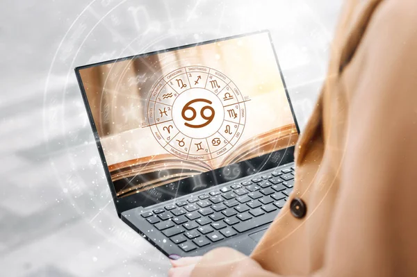 Astrological forecast for the zodiac sign cancer. Woman holding an open laptop with a picture of a book and the zodiac circle. future prediction