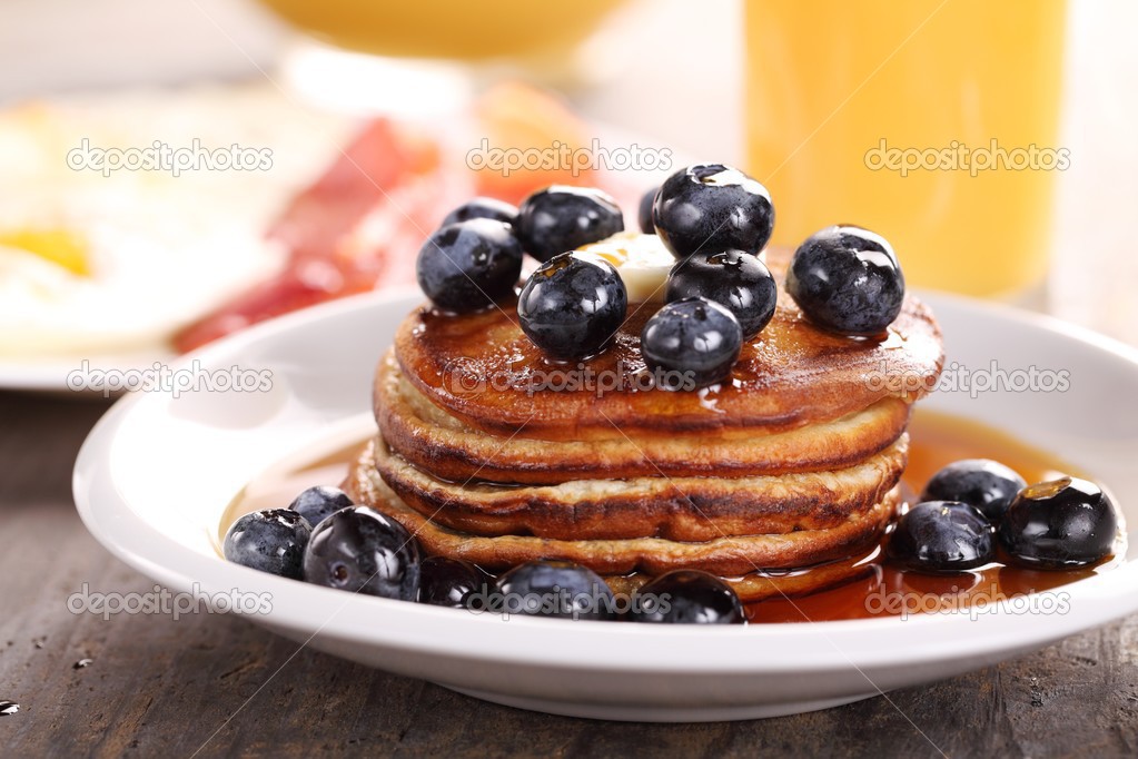 Plate with pancakes, juice and eggs with bacon.