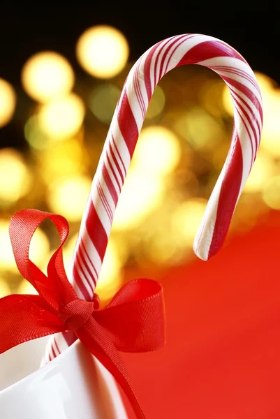 Candy cane with red ribbon on holiday lights — Stock Photo, Image