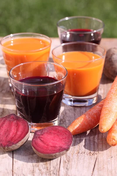 Glas met rode biet en wortel sap op tuinmeubelen. — Stockfoto