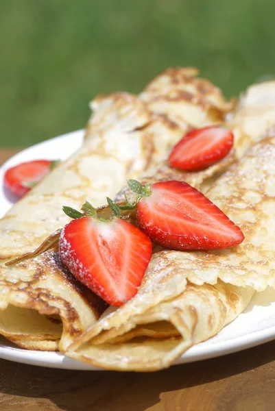 Sweet crepes with strawberries on garden table — Stock Photo, Image