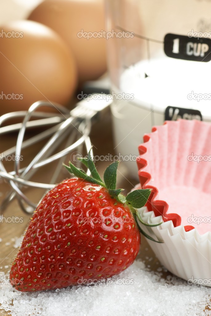 Cupcakes, strawberry, eggs, whisk and measuring cup with milk.
