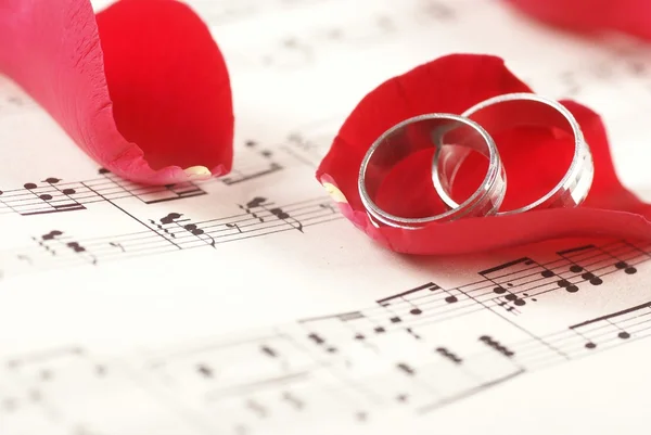 Two rings on music notes with red rose petals. — Stock Photo, Image