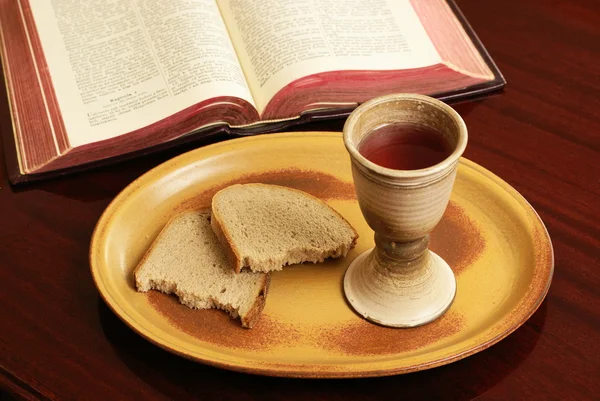 Kalich, chléb a otevřené Bibli na stůl. — Stock fotografie