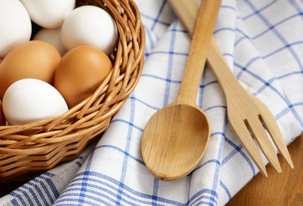 Detalle de canasta de mimbre con huevos de pollo, cuchara de madera, tenedor y paño de cocina — Foto de Stock