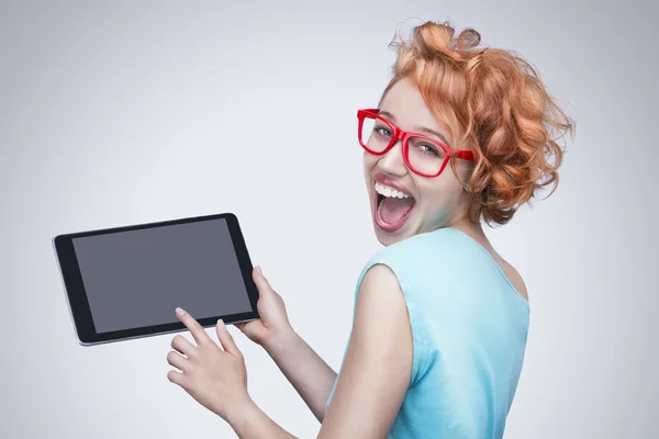 Chica de pelo rojo emocional con gafas rojas sosteniendo y tocando la computadora tableta . — Foto de Stock