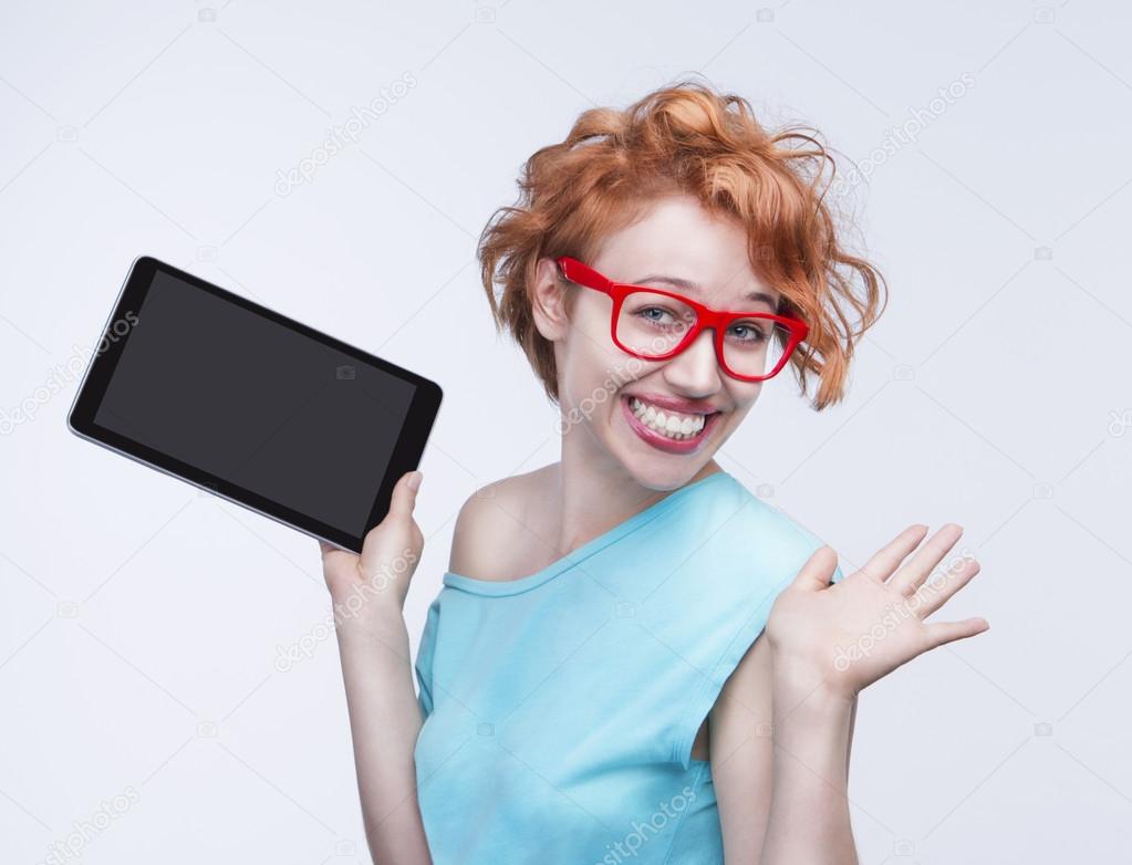 Emotional cute red-haired girl holding tablet computer, opening hands.