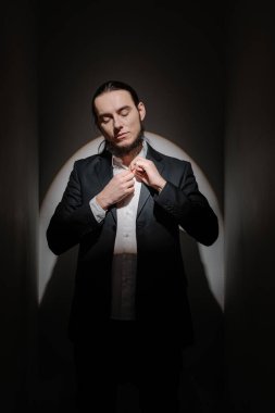 Gömleğinin düğmelerini ilikleyen şık takım elbiseli, sakallı yakışıklı, aşağı bakıyor. Damat parti akşamına hazırlanıyor. Zarif bir siyah-beyaz simetrik kompozisyon. Egoist ruh hali