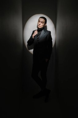 Egoist bakış. Sakallı zarif takım elbiseli genç adam kibirli bir şekilde yan tarafa bakıyor. Sahne ışıkları tiyatro havasında. Bencil kibirli, kendine güvenen davranış. Zarif biçim siyah ve beyaz simetrik bileşimi