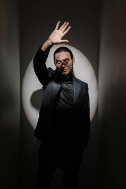 Sakallı, uzun saçlı, şık bir adam yüzünü ışıktan koruyor. Elini öne uzat. Yüzün gölgesi elle tutulur. İnkar, dur ya da önleme konsepti. Sahne ışıkları tiyatro atmosferi