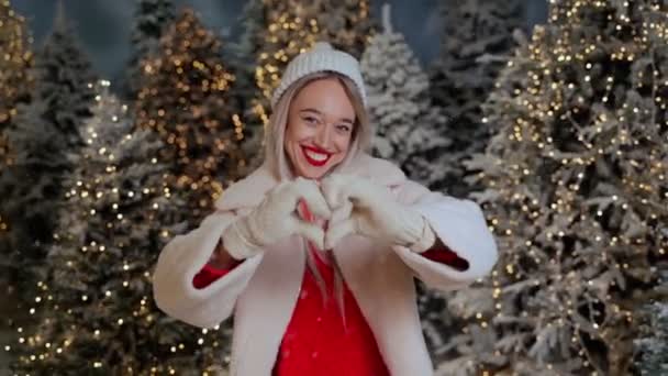 爱情就在空气中 金发碧眼的女人住在白雪覆盖的森林里 树上点缀着灯光 展示内心的手浪漫的象征 白色手套和红色套头毛衣 冬季日期 — 图库视频影像