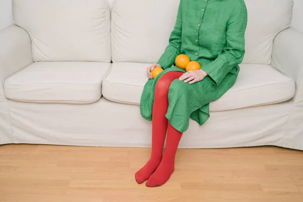 Vestido Verde Meias Vermelhas Mulher Sentada Sofá Bege Segurando Laranjas — Fotografia de Stock