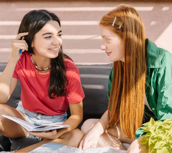 discussion, planning, making notes and working (studying) together. Having fun and laughing. Two young girls friends looking to each other and making notes. Sunny summer terrace. Red and green