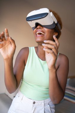 portrait of African American girl playing VR game at home, copy space. Exited using vr glasses, watching 360 degree video  with virtual reality headset looking up. Vertical composition
