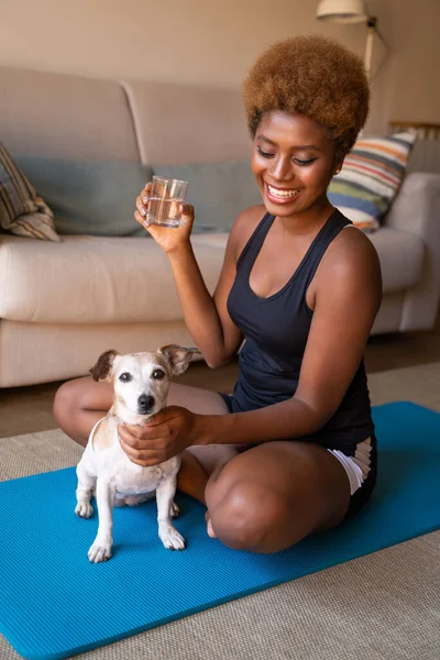 Happy morning routine sports and water. beautiful young woman drinking water petting small white dog sitting next to her. hydration