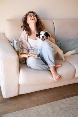 Gülen güzel bir kadın elinde kitapla kanepede oturur ve bir komedi romanı okur. Köpek kucağında, rahatlamış hafta sonu havasına bakıyor. Güneşli aydınlık oturma odası gündüz vakti