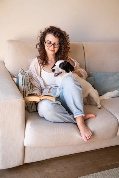 Gyönyörű Göndör Lány Szemüveggel Kanapén Könyvvel Fekete Fehér Örökbefogadott Kutyájával — Stock Fotó