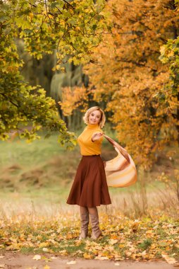 Yaşlı bir kadın, bir sonbahar parkında sarı yapraklardan oluşan bir arka plana doğru dönüyor. Hayatın tadını çıkarıyorum.